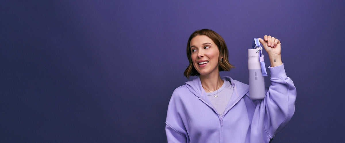 Millie Bobby Brown is holding the florence by mills x BRITA LARQ bottle on purple background.