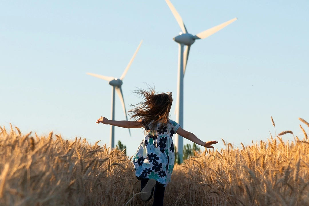 Girl running through a field of grass with wind turbines in the background.