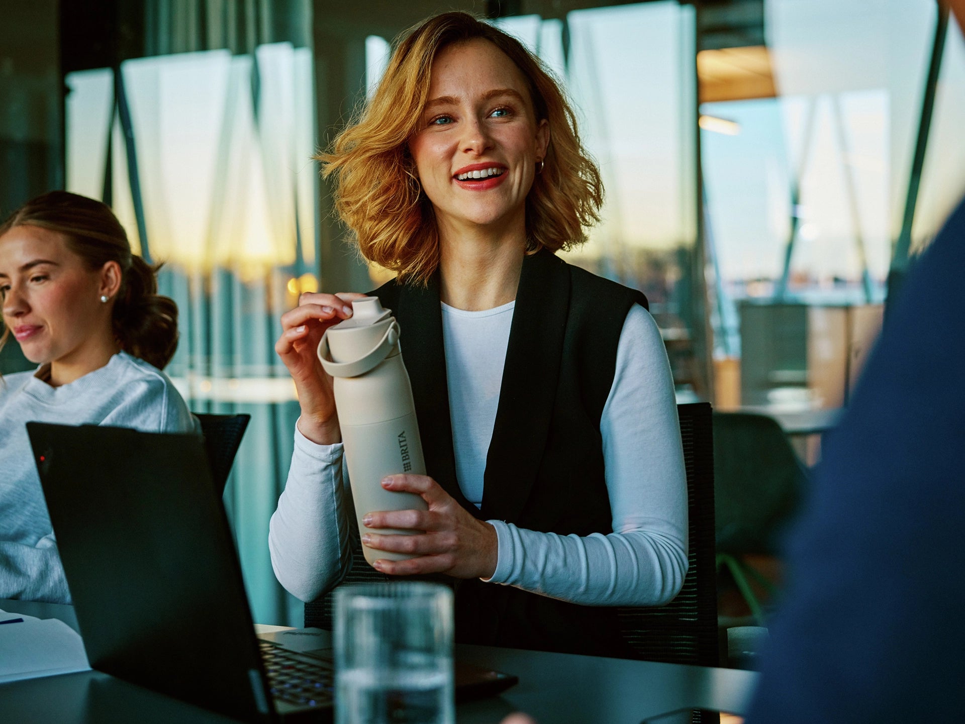 Woman in office with laptop helds a beige BRITA LARQ water filter bottle.