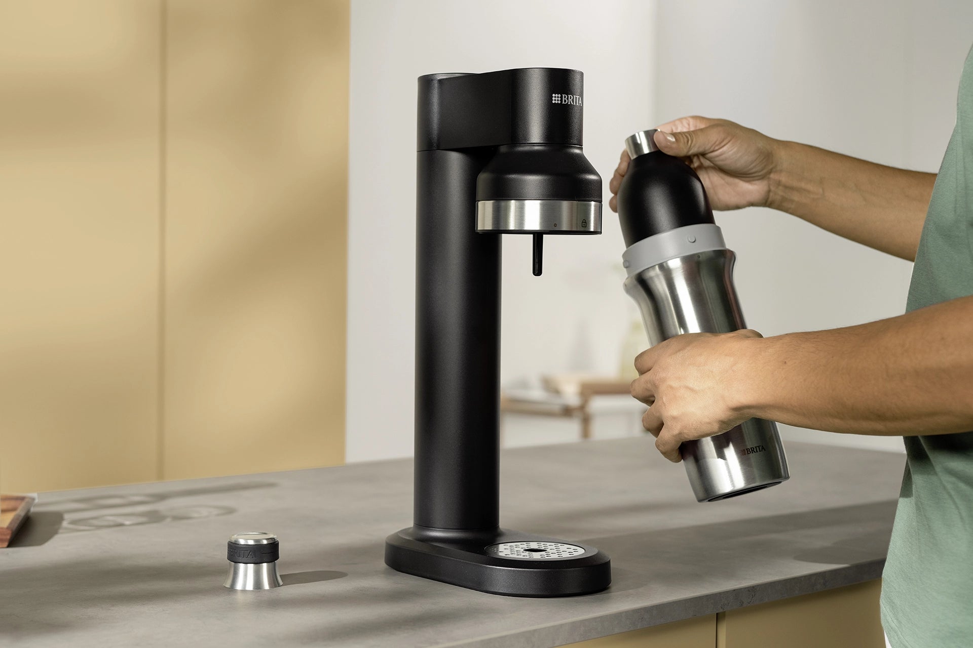 Person inserting a BRITA sodaTRIO Stainless Steel Bottle into a black BRITA sodaTRIO Sparkling Water Maker.