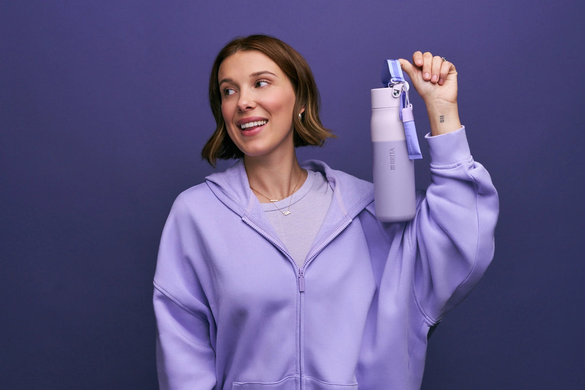 Millie Bobby Brown smiling and is holding the florence by mills x BRITA LARQ bottle on purple background.