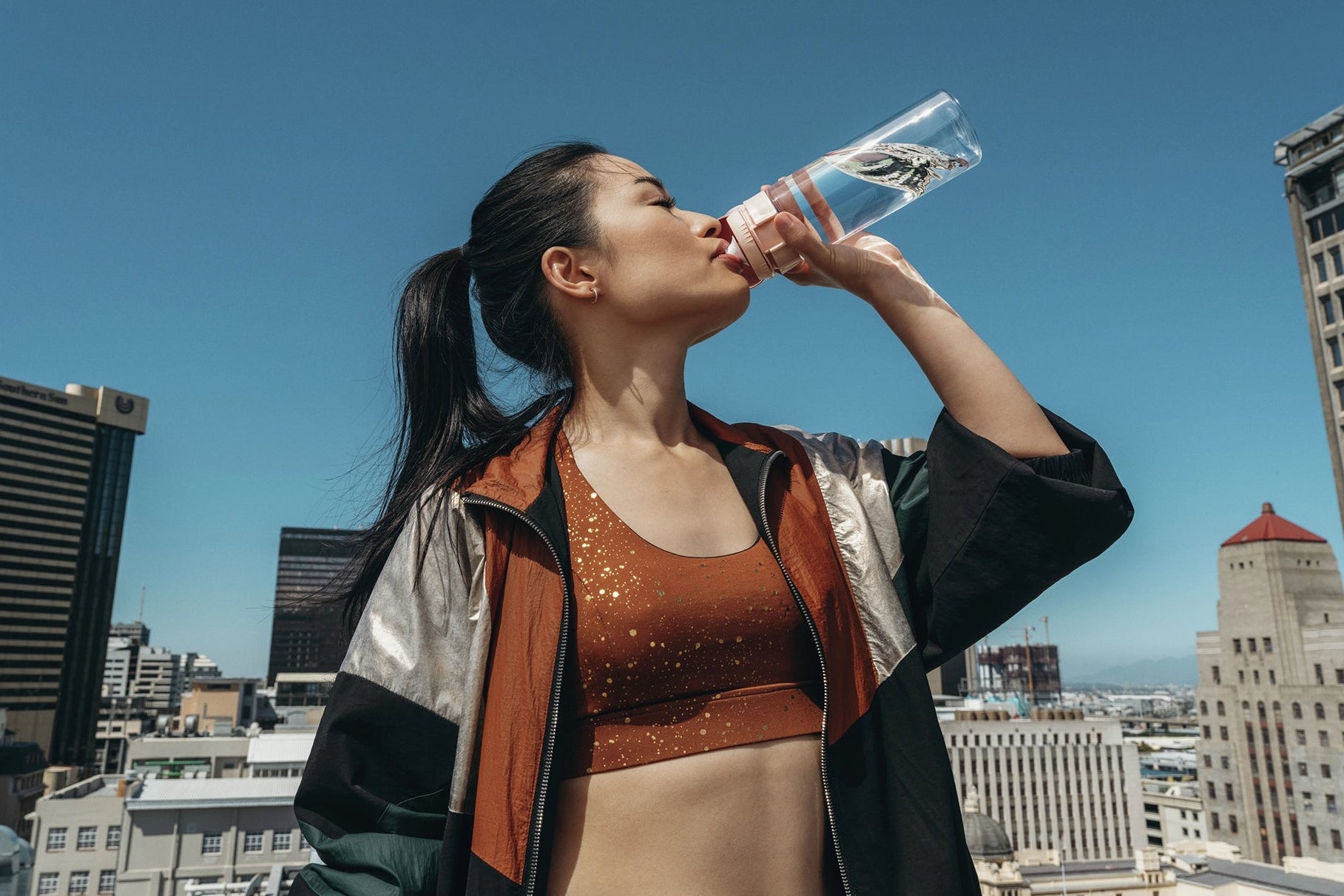 Woman drinking from a BRITA Water Filter Bottle Model Vital with a city skyline in the background.