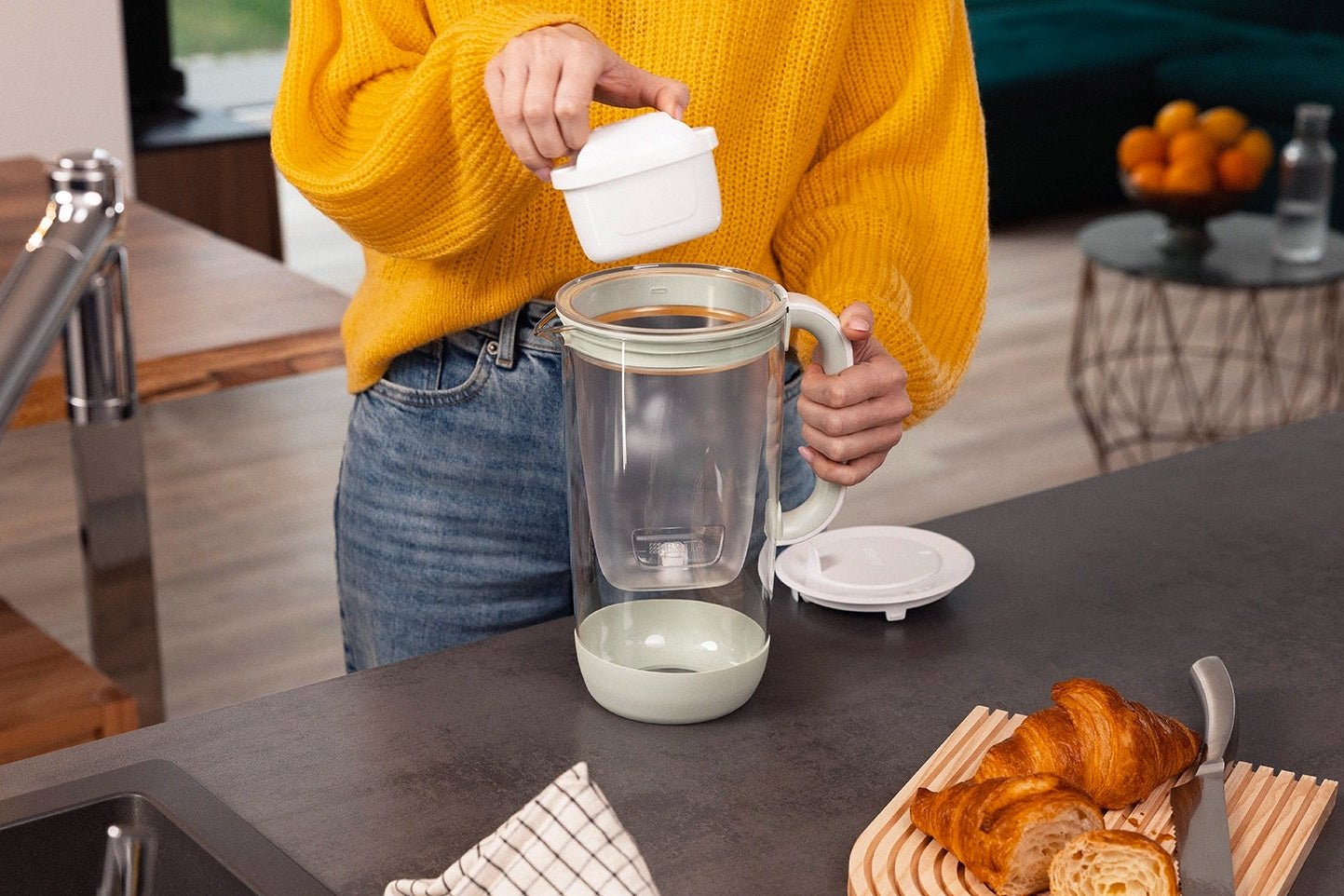 Person inserting a MAXTRA PRO filter cartridge into the BRITA Glass Jug in a modern kitchen.