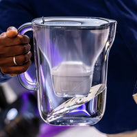 Person holding a blue BRITA Style Essential water filter jug filled with water.