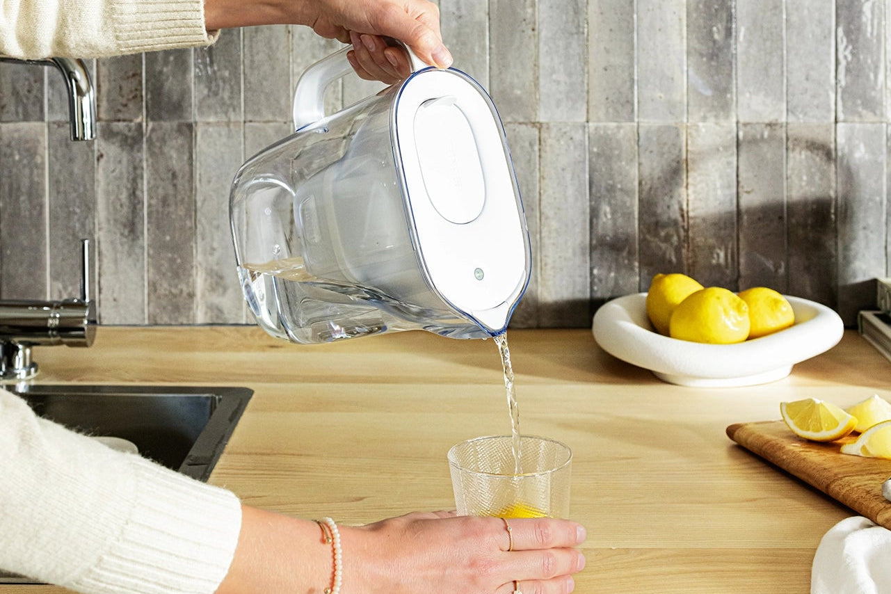Person pouring water from a white BRITA Style Essential into a glass on a kitchen counter.