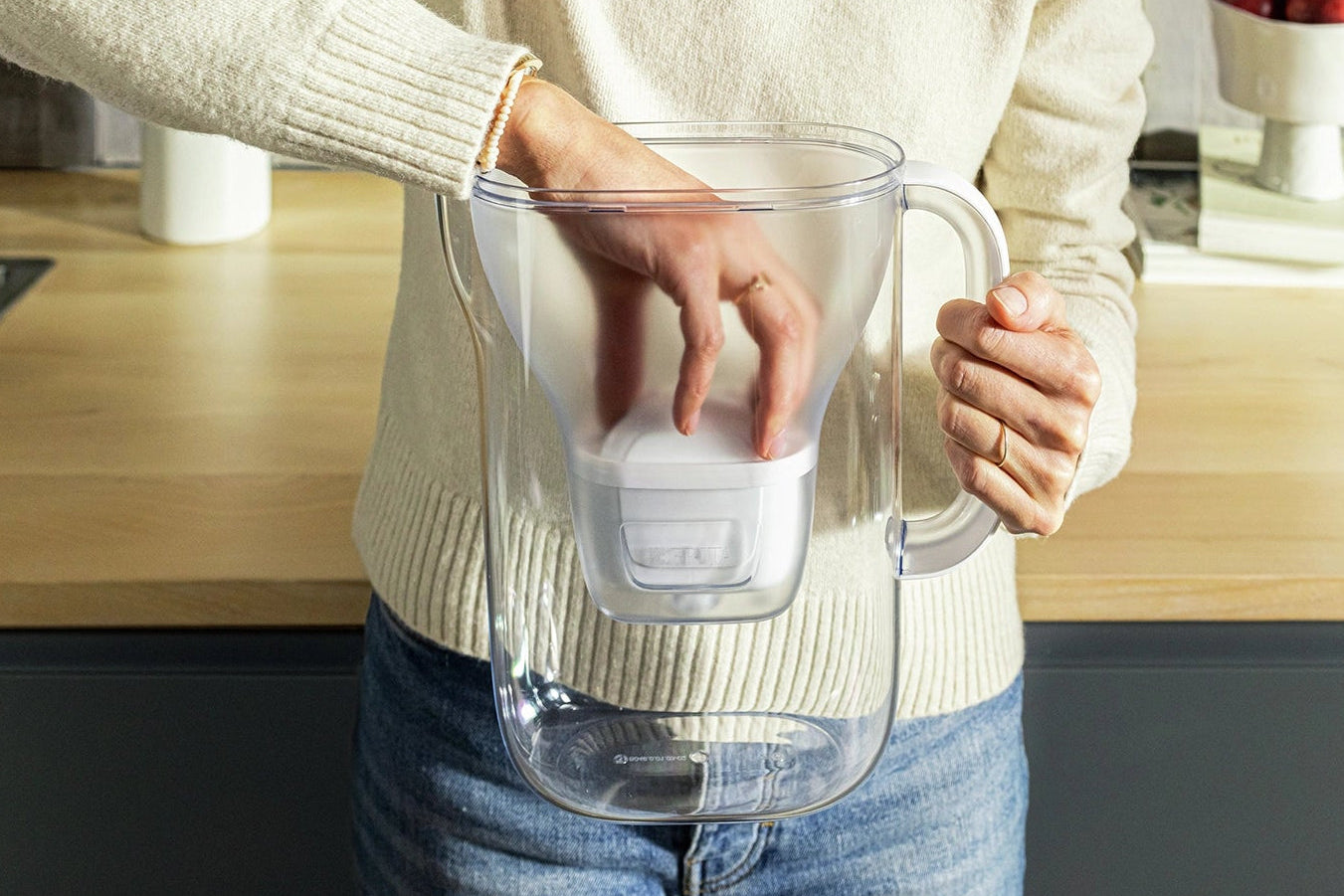 Person in a white sweater inserting a MAXTRA PRO filter cartridge into a BRITA Style Essential water filter jug.