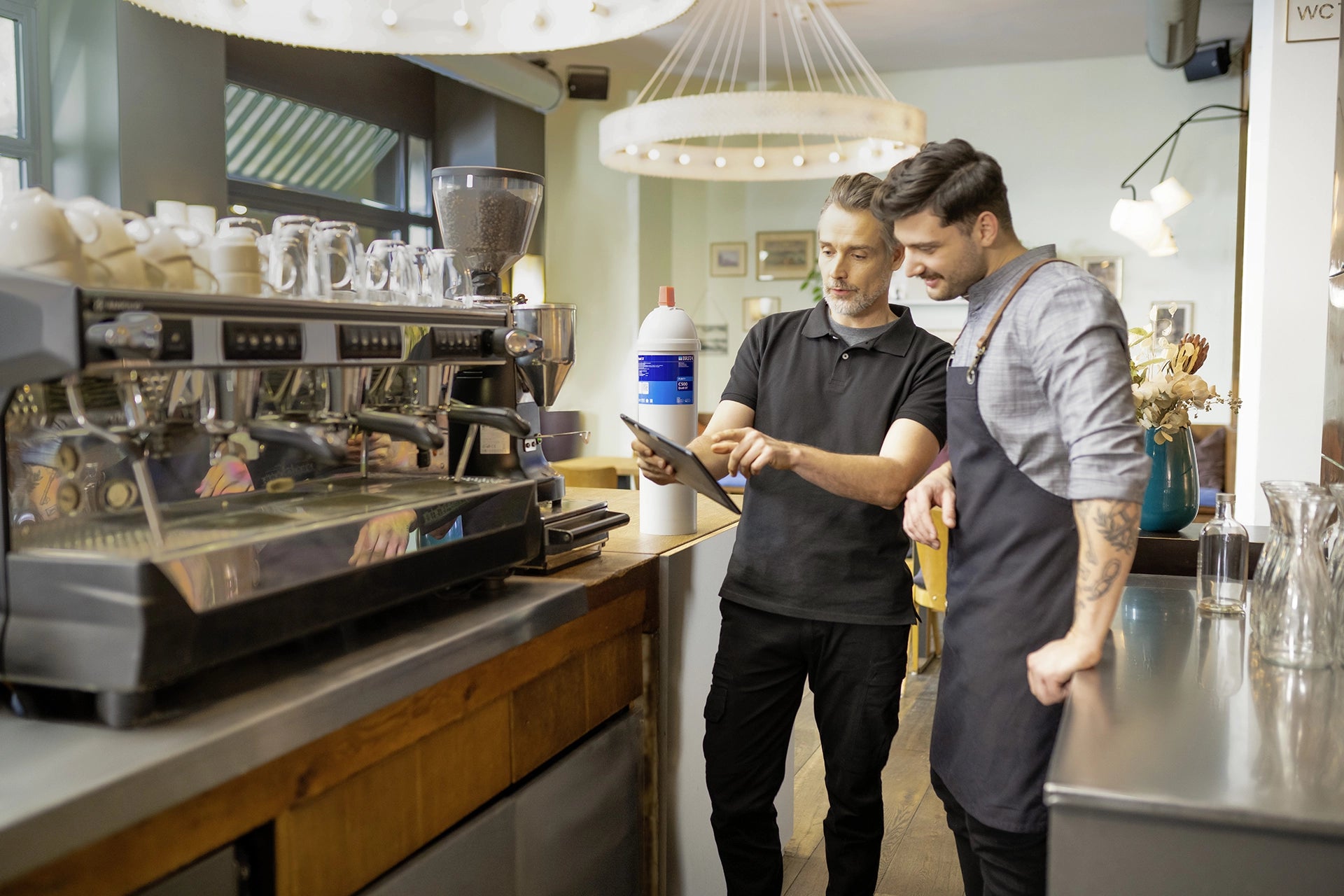 Coffee machine and BRITA Professional filter cartridge with two people reviewing information on a tablet in a café